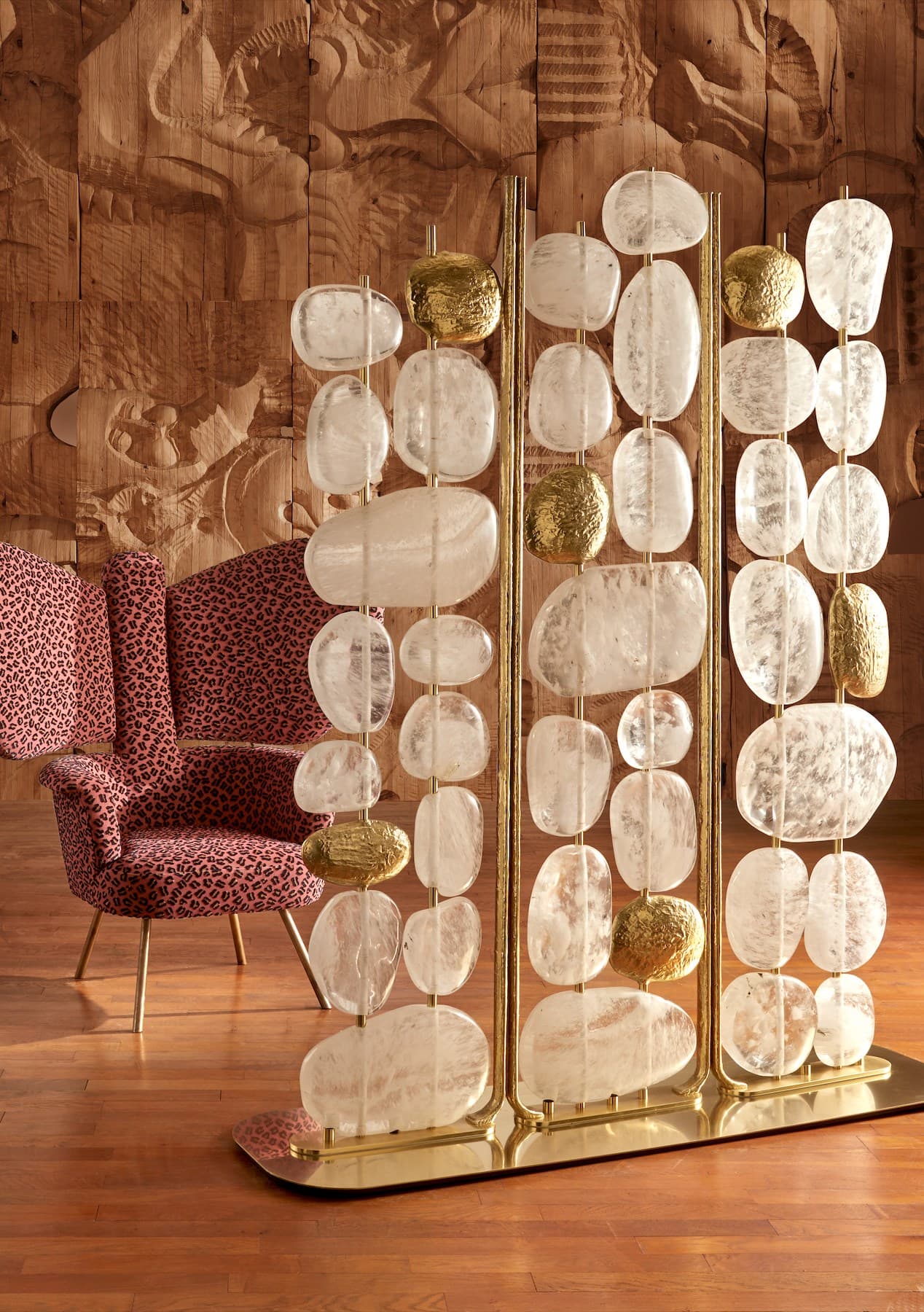 A decorative room divider composed of multiple vertical brass rods supporting strings of translucent, flattened oval-shaped stones and textured, pebble-like golden accents. The stones appear to be natural, possibly quartz or agate, exhibiting variations in translucency and internal inclusions. The brass frame provides a vertical structure, with a rectangular base plate. — 3D model