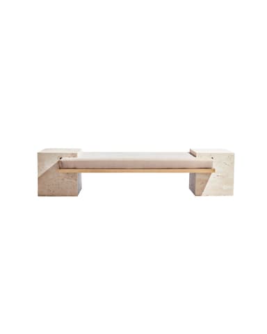 A modern bench featuring two substantial, rectangular stone block legs supporting a cushioned seat. The legs appear to be made of travertine or a similar porous, light-colored stone, with visible natural pitting. A thin, rectangular metal frame, likely brass or a similar golden-toned metal, spans between the legs and supports the seat cushion. The seat cushion is upholstered in a plain, light-colored fabric. — 3D model