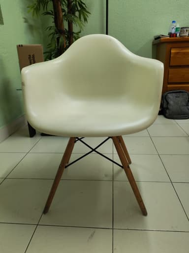 An off-white, molded plastic armchair with integrated armrests and a 'Eiffel Tower' style base consisting of splayed wooden dowel legs reinforced with black metal cross-supports. The chair is positioned on a light-colored tiled floor. — 3D model
