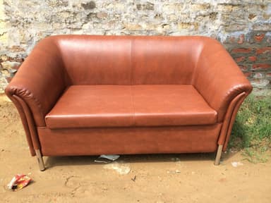A two-seater sofa upholstered in brown leather. It features a curved back and armrests, with subtle vertical stitching details on the sides of the armrests. The sofa is supported by four slender, cylindrical metal legs. — 3D model
