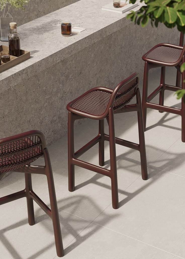 A contemporary bar stool constructed from molded plastic, featuring a slatted backrest and seat. The stool has a dark brown or espresso color and includes an integrated footrest connecting its four legs. The design is minimalist and modern, suggesting suitability for both indoor and outdoor use. — 3D model