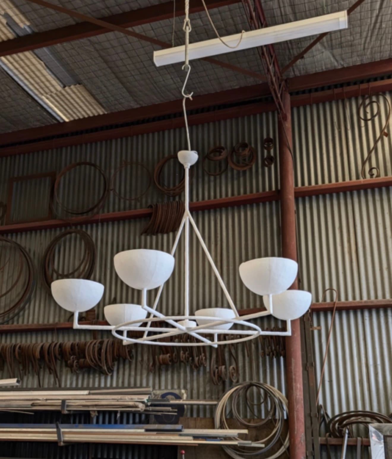 A modern white five-light chandelier featuring a geometric metal frame and five bowl-shaped shades. The fixture is suspended from a central rod and chain, culminating in a simple ceiling canopy. Each light source is housed within an opaque hemispherical shade, directing light upwards or outwards depending on the shade's orientation. The overall design emphasizes clean lines and a contemporary aesthetic. — 3D model