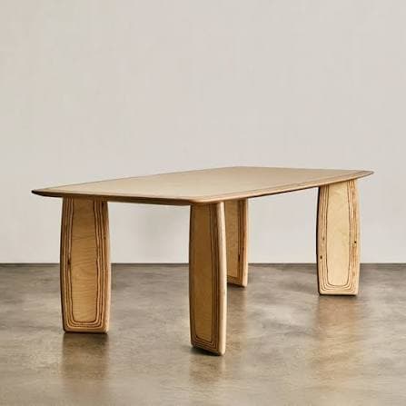 A rectangular dining table crafted from light-colored plywood, featuring a smooth tabletop with gently rounded corners and thick, curved slab-like legs that display the layered construction of the wood. — 3D model