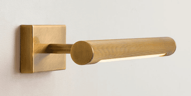 A horizontal, elongated wall-mounted LED light fixture, crafted from brass or a brass-toned metal. The main cylindrical body features a distinct ribbed texture and emits light from a continuous strip along its bottom edge. It is affixed to the wall by a rectangular mounting plate, creating a minimalist and functional aesthetic. — 3D model
