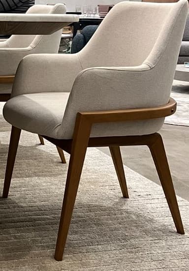 A modern upholstered armchair featuring a curved backrest and integrated armrests, supported by a visible wooden frame and four tapered legs. The upholstery is a light, neutral fabric, and the wooden frame has a medium brown finish. — 3D model