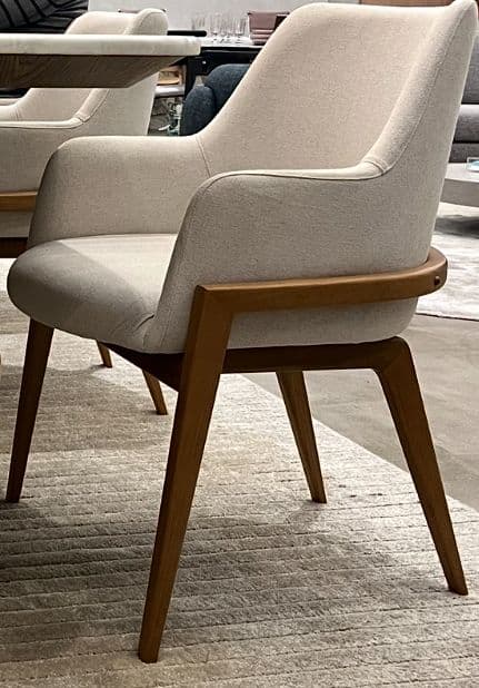 A modern upholstered armchair featuring a curved backrest and integrated armrests, supported by a visible wooden frame and four tapered legs. The upholstery is a light, neutral fabric, and the wooden frame has a medium brown finish. — 3D model