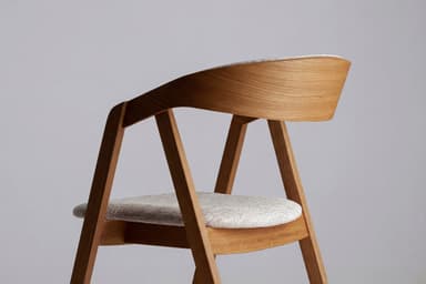 A modern armchair constructed from light-toned wood, featuring a curved backrest that flows into integrated armrests. The seat is an upholstered pad covered in a light grey textured fabric. — 3D model