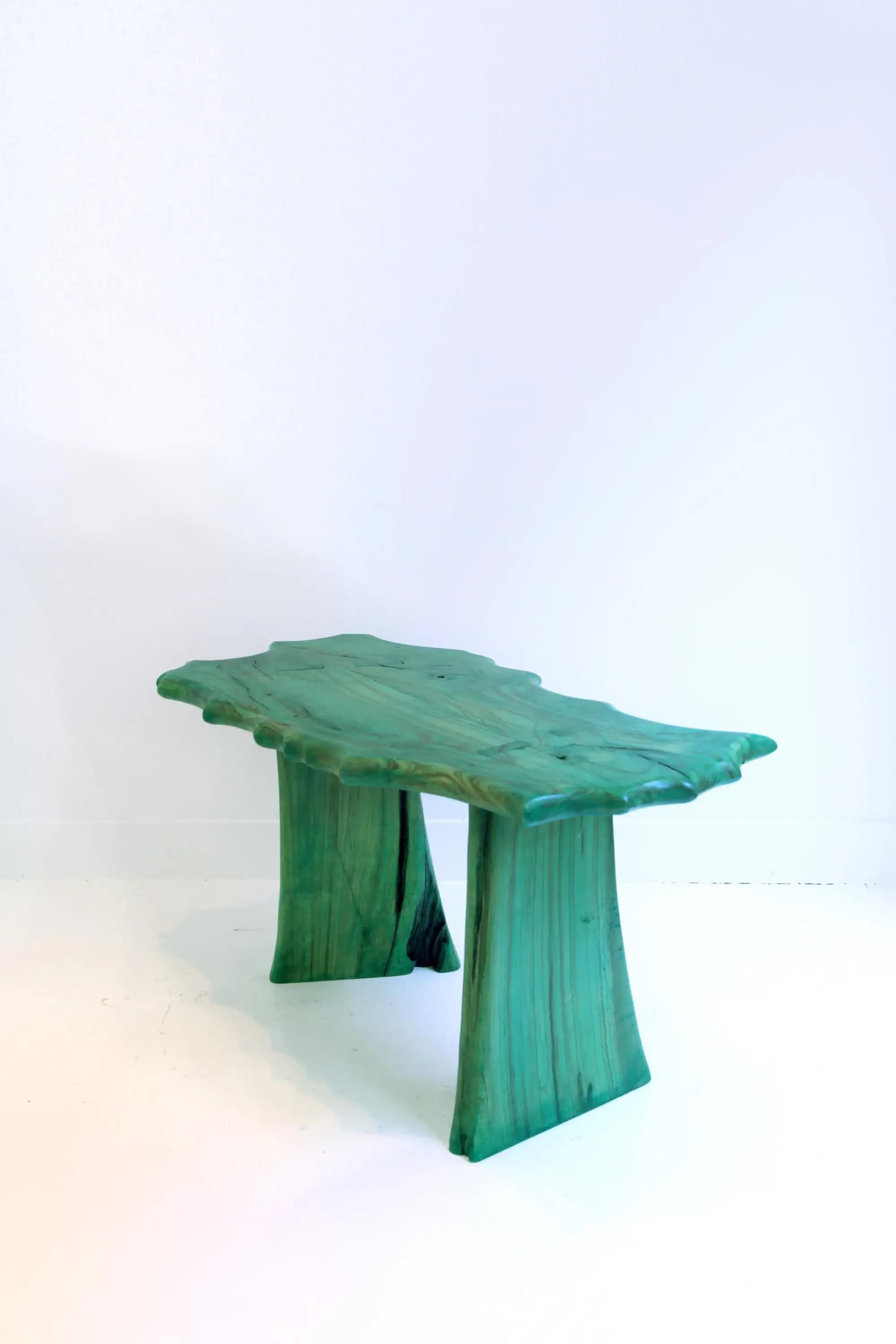 A sculptural console table featuring a vibrant green finish and an organic, irregular live edge tabletop, supported by two thick, irregularly shaped legs. The material appears to be wood or a wood-like resin with visible striations or grain. — 3D model