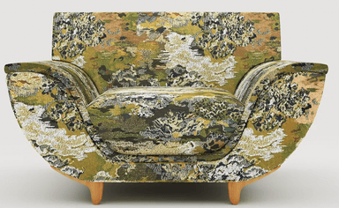 A single armchair upholstered in a textured fabric with a dense, abstract pattern featuring shades of green, brown, and white. The armchair has a rounded back and arms, with a prominent seat cushion. It is supported by four slender, tapered wooden legs. — 3D model