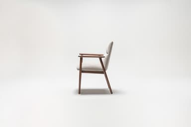 A side profile view of a mid-century modern armchair against a plain white background. The armchair features a wooden frame with dark brown legs and armrests. The seat and back are upholstered in a light-colored textured fabric. — 3D model