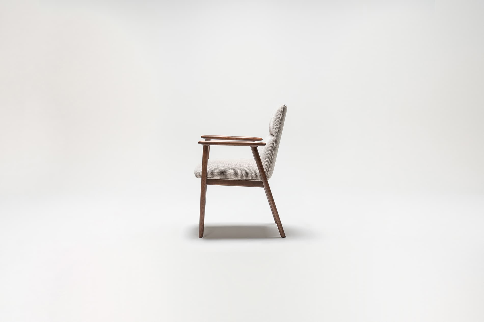 A side profile view of a mid-century modern armchair against a plain white background. The armchair features a wooden frame with dark brown legs and armrests. The seat and back are upholstered in a light-colored textured fabric. — 3D model