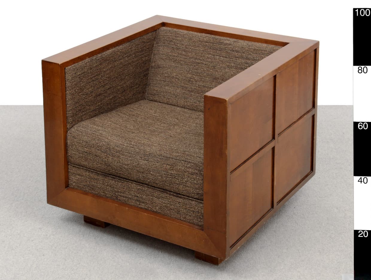 A single armchair with a wooden frame and upholstered seat and back. The frame has a cubic structure with straight lines, featuring inset panels on the exterior sides. The upholstery is a textured fabric in a brown hue. — 3D model