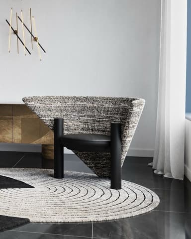 A modern armchair featuring a distinctive, wide, fan-shaped backrest upholstered in a speckled black and white textured fabric. The circular seat cushion is upholstered in smooth black material, likely leather or faux leather. The chair is supported by two thick, cylindrical black posts that serve as both legs and structural support, creating a striking visual contrast with the enveloping backrest. — 3D model