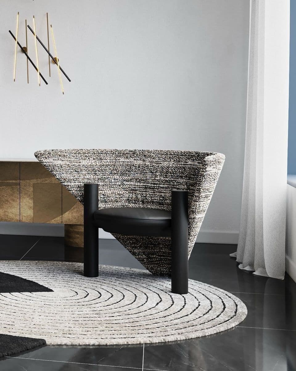 A modern armchair featuring a distinctive, wide, fan-shaped backrest upholstered in a speckled black and white textured fabric. The circular seat cushion is upholstered in smooth black material, likely leather or faux leather. The chair is supported by two thick, cylindrical black posts that serve as both legs and structural support, creating a striking visual contrast with the enveloping backrest. — 3D model