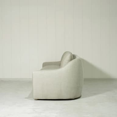 A three-seater sofa with a curved armrest on the left side. The sofa has a tailored base and three seat cushions. The back features three distinct cushions, all upholstered in a light-colored, textured fabric. — 3D model