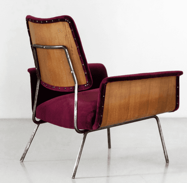 A modern armchair with a distinct mid-century aesthetic. It features a curved backrest and seat upholstered in a deep burgundy, possibly velvet or a similar textured fabric. The armrests are integrated into the main body of the chair. A prominent design element is the exposed wooden panel on the sides, appearing to be bent plywood, which contrasts with the upholstered sections. The chair is supported by slender, metallic legs that angle outwards. — 3D model