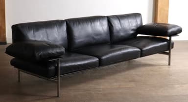 A modern three-seater sofa upholstered in black leather, featuring a minimalist design with a visible slim metal frame. It has three individual seat cushions, three back cushions, and detached, cushioned armrests, all in matching black leather. The sofa stands on slender metal legs, contributing to its sleek, elevated profile. — 3D model