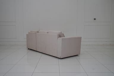 A sectional sofa with a chaise lounge extension, upholstered in a light-colored fabric with a subtle pattern. The sofa features three seat cushions and a chaise on the right side. It includes four matching throw pillows. The sofa has a modern, minimalist design with clean lines and low-profile arms and back. — 3D model