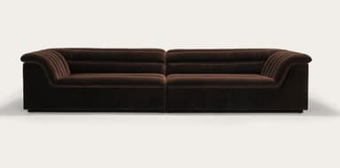 A long, three-seater sofa with a channeled design on the backrests and armrests. The sofa appears to be upholstered in a plush fabric and features a low profile with a distinct armrest that curves outwards. — 3D model