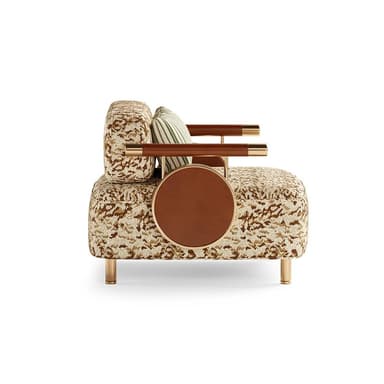 An avant-garde accent armchair featuring a patterned fabric upholstery in shades of beige and brown, lending an eclectic and luxurious aesthetic. The chair incorporates unique armrests made of polished brass rods wrapped with brown leather, which extend to support a circular, integrated side table on one side, also finished in brown leather and framed in brass. It is supported by four slender, tapered brass legs, suggesting a modern yet opulent design. — 3D model