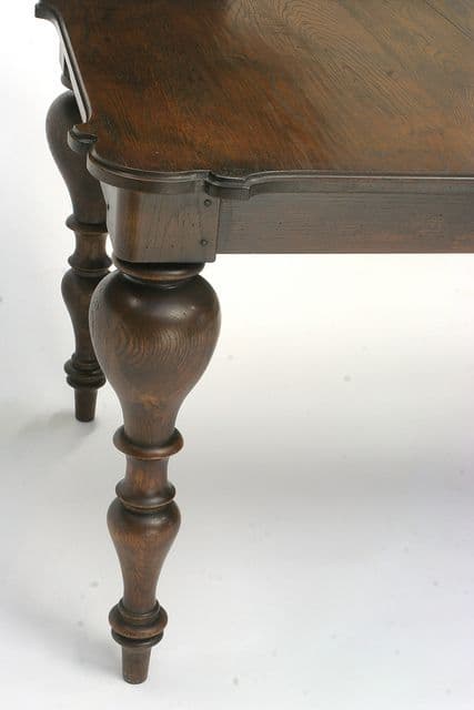 A close-up view of a traditional dark wood table, likely a dining table, showcasing its ornate turned leg and the scalloped profile of the tabletop. The wood has a visible grain and a deep brown finish. — 3D model