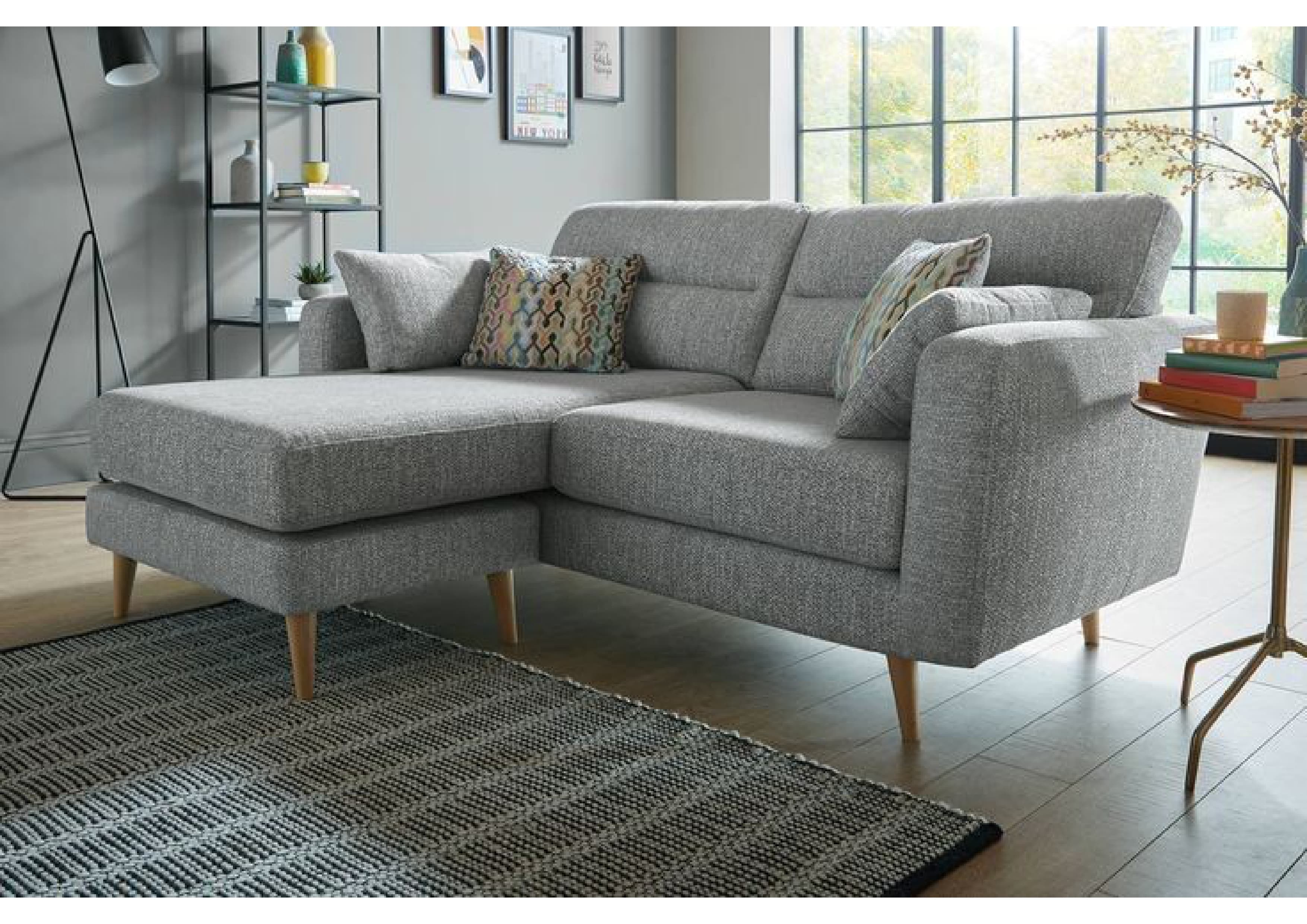 A modern sectional sofa upholstered in light grey fabric, featuring a left-hand chaise extension, supportive back cushions, and slender wooden legs, accompanied by two decorative throw pillows. — 3D model