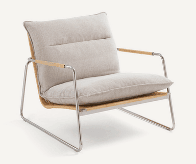 A low-profile modern lounge chair featuring a sleek, polished tubular steel frame. The seat and backrest are constructed from tightly woven natural cane, providing a textured, organic element. Thick, light-colored fabric cushions rest on the cane surfaces for comfort. The integrated armrests are part of the continuous steel frame, with a wrapped detail on the top sections. — 3D model