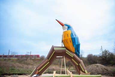 A decorative sculpture depicting a kingfisher bird perched on a branch, crafted from multiple segmented pieces of wood. The bird features a vibrant blue, orange, and white palette, while the branch is predominantly brown with green and lighter brown accents, all finished with a smooth, glossy appearance. — 3D model
