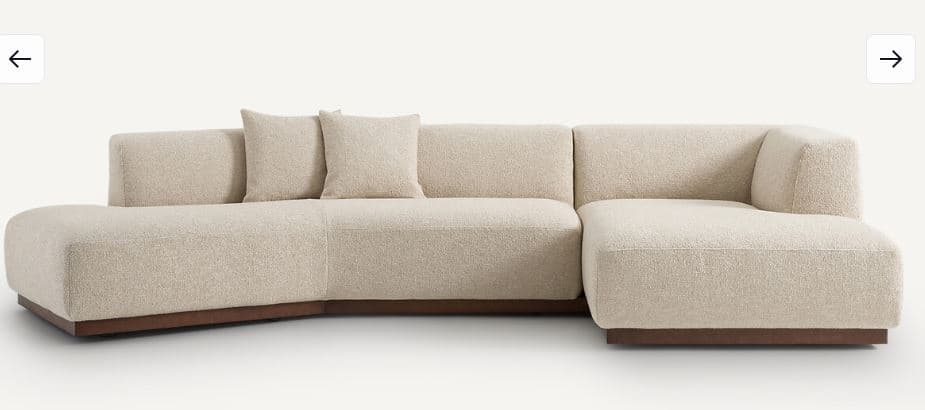 A modular sectional sofa with a low profile and clean lines. The sofa features a textured fabric upholstery and a dark wood base. It is configured with a chaise lounge on the left and a corner section on the right, accompanied by two square throw pillows. — 3D model