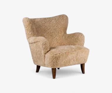 A light brown, sheepskin-upholstered armchair featuring a distinctive wingback silhouette and four dark wooden tapered legs. The chair presents a plush, textured surface that appears soft and inviting. Its design includes gently curved lines and rounded armrests, suggesting a comfortable and enveloping form, all in excellent condition. — 3D model