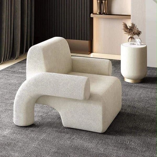 An off-white, upholstered accent chair featuring a contemporary, sculptural design with an asymmetrical form. One armrest is a solid, block-like extension of the seat back, while the other is a distinctive, C-shaped curved element that meets the floor. The entire piece is covered in a textured bouclé fabric, presenting a monolithic and plush appearance. — 3D model