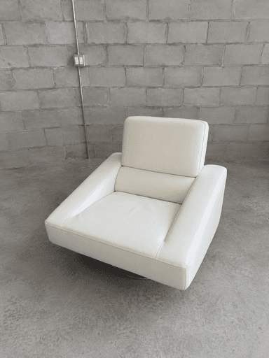 A contemporary white upholstered lounge chair featuring a low-profile design, broad rectangular armrests, and a hidden swivel base. The seating and back cushions are well-padded, providing a plush yet structured appearance. The upholstery material appears to be a smooth, off-white leather or high-quality faux leather, with precise stitching details. — 3D model
