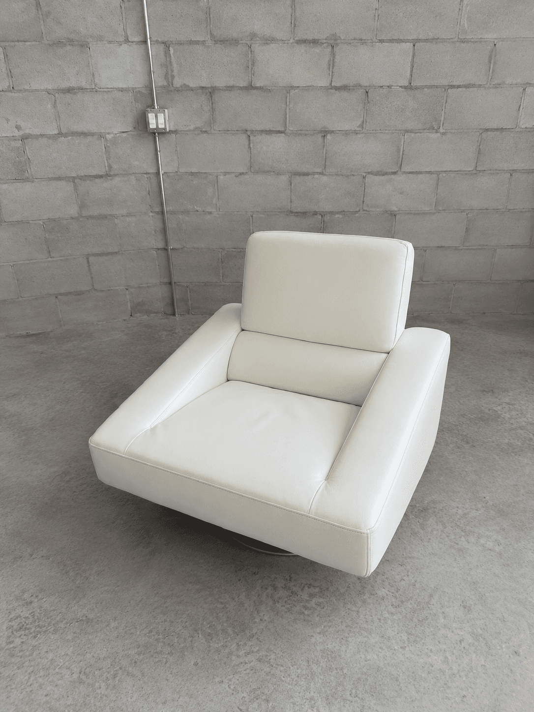 A contemporary white upholstered lounge chair featuring a low-profile design, broad rectangular armrests, and a hidden swivel base. The seating and back cushions are well-padded, providing a plush yet structured appearance. The upholstery material appears to be a smooth, off-white leather or high-quality faux leather, with precise stitching details. — 3D model
