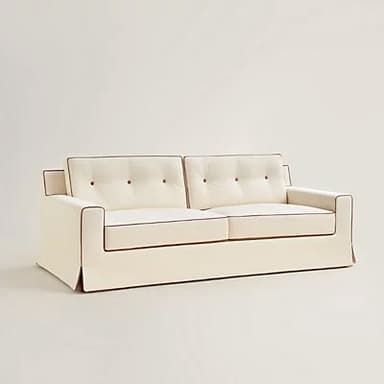 A white sofa with tufted back cushions and contrasting dark piping along the edges of the cushions and arms. The sofa features a skirted base and a clean, modern design. — 3D model