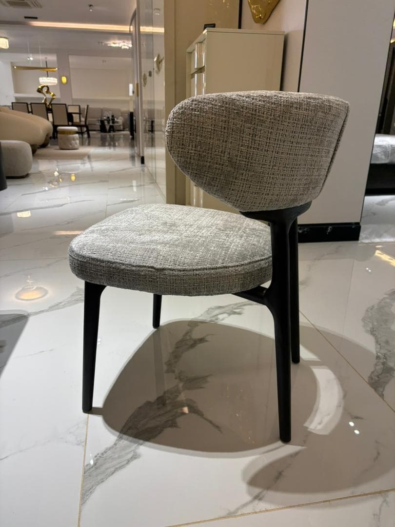 A modern upholstered chair with a curved backrest and a seat. The chair has four tapered legs and appears to be made of wood or metal with a dark finish. The upholstery is a textured fabric in a neutral tone. — 3D model