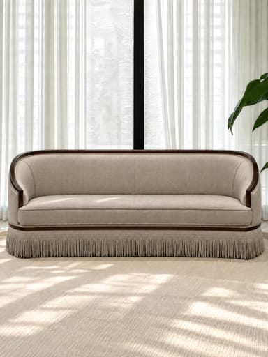 A traditional barrel back sofa featuring a continuous curved back and arms, an exposed dark wood frame, light neutral fabric upholstery, a single seat cushion, and a decorative fringe skirt. — 3D model