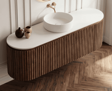 A contemporary wall-mounted bathroom vanity featuring a fluted wood cabinet, a white solid surface countertop, and a cylindrical white vessel sink, complemented by brass wall-mounted faucets. — 3D model