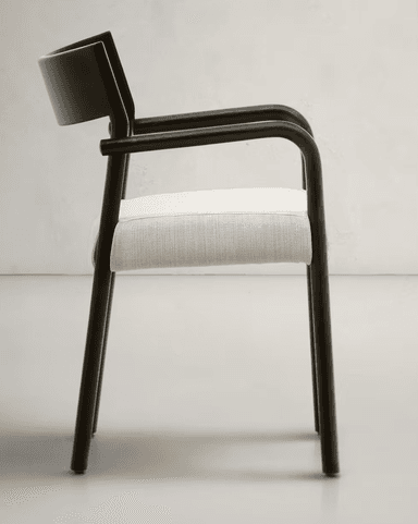 A modern armchair featuring a dark, matte-finished frame with a curved backrest and arms. The seat is upholstered in a light-colored, textured fabric. The legs are slender and cylindrical, matching the frame's finish. The design emphasizes clean lines and a minimalist aesthetic. — 3D model