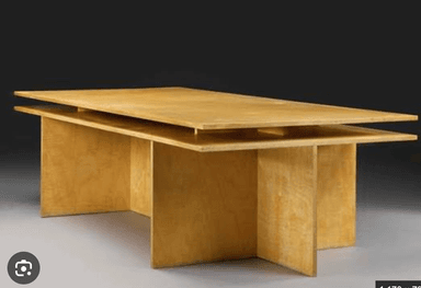 A minimalist desk constructed from light-colored plywood, featuring a distinctive floating top design. The desk is supported by two solid panel legs on the sides and a central full-height panel that also functions as a modesty panel. The layered edges of the plywood are visible, enhancing its modern aesthetic. — 3D model