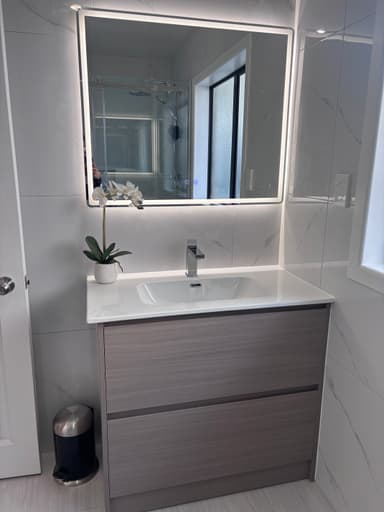 A modern wall-mounted bathroom vanity unit featuring a rectangular white integrated sink and countertop. The base cabinet has two handleless doors with a horizontal light wood grain finish. A chrome single-handle faucet is mounted on the countertop. — 3D model