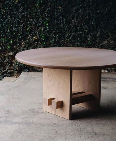 A low, round table crafted from light-colored wood, featuring a thick circular top supported by a sturdy, block-like base with visible, protruding joinery elements, suggesting a minimalist and craft-inspired design. — 3D model