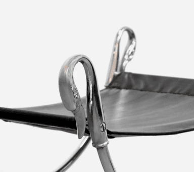 A polished chrome-plated metal and black leather X-frame stool, featuring a sling-style seat and decorative swan-head finials on the frame. — 3D model