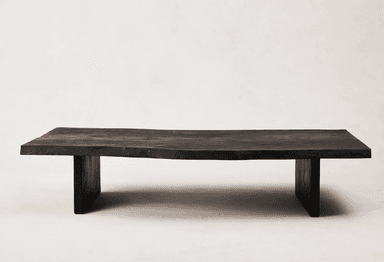 A low, rectangular coffee table with a live-edge top and thick, blocky legs. The tabletop has an irregular, natural edge on one side, and the surface displays visible wood grain. The legs are positioned inset from the ends of the tabletop. — 3D model