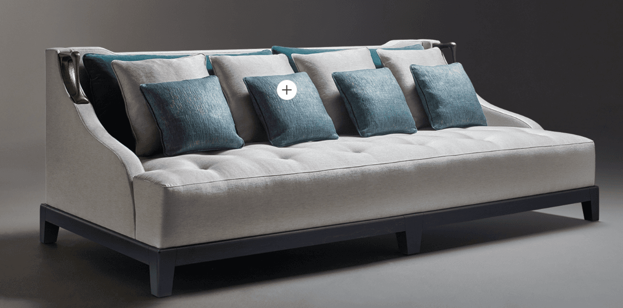 An elegant contemporary daybed featuring a light grey upholstered frame with a low back and integrated side panels, accented with decorative brass-toned metal pieces. The deep seat is button-tufted and accompanied by a set of varying sized bolster and throw cushions in teal and light grey, providing comfortable back support. It rests on a dark, geometric wooden base with block feet. — 3D model