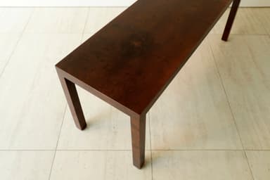 A long, narrow, dark brown console table with a minimalist design, featuring a rectangular top and four straight, thick legs integrated seamlessly into the corners, resting on a light tiled floor. — 3D model