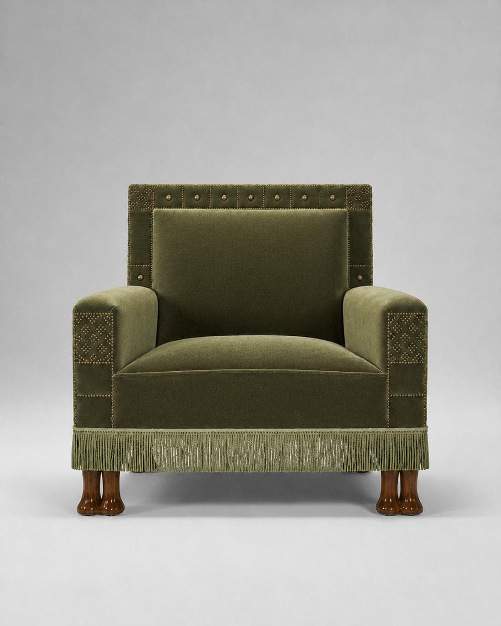 An armchair upholstered in a textured green fabric, featuring decorative brass studs along the edges of the backrest and armrests. The armchair has a straight back, wide arms, and a seat cushion. It is finished with a fringe skirt at the base and stands on four carved wooden feet. — 3D model