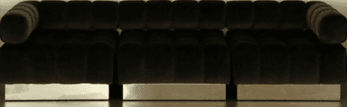 A long, contemporary modular sofa featuring deep channel tufting across all upholstered surfaces, including the backrest and armrests. The sofa is upholstered in a dark, possibly velvet or chenille, fabric and sits on a low, polished metallic base. — 3D model