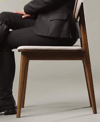 A contemporary dining chair featuring a solid oak wood frame with a clear, light-brown finish and a subtly curved wooden backrest. The seat is upholstered in a light beige, textured fabric. The chair stands on four sturdy, tapered wooden legs, with visible wood grain throughout the frame, suggesting a natural and minimalist design. — 3D model