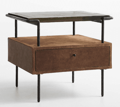 A nightstand featuring a distressed brown leather-wrapped body with a single drawer, supported by a black industrial-style metal frame and legs. The top surface is an olive green, textured material, possibly stone or a stone-look composite, which sits within the metal frame. An open shelf is present above the drawer. — 3D model