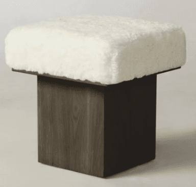 A contemporary square ottoman featuring a thick, plush, white boucle upholstered top, supported by a minimalist dark wood cube base with a visible grain texture. — 3D model